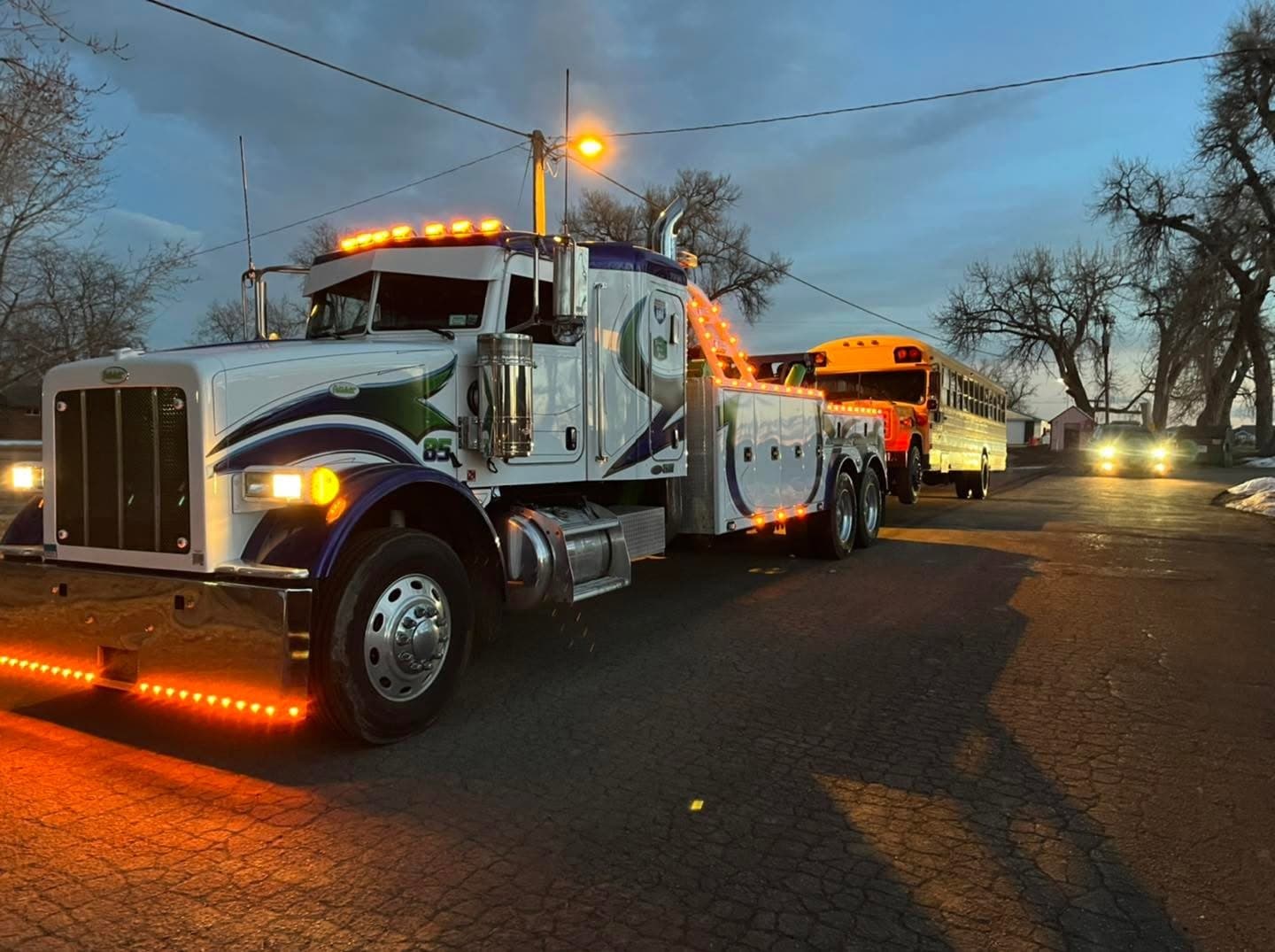 Wrecker on the shoulder at dusk with lights on