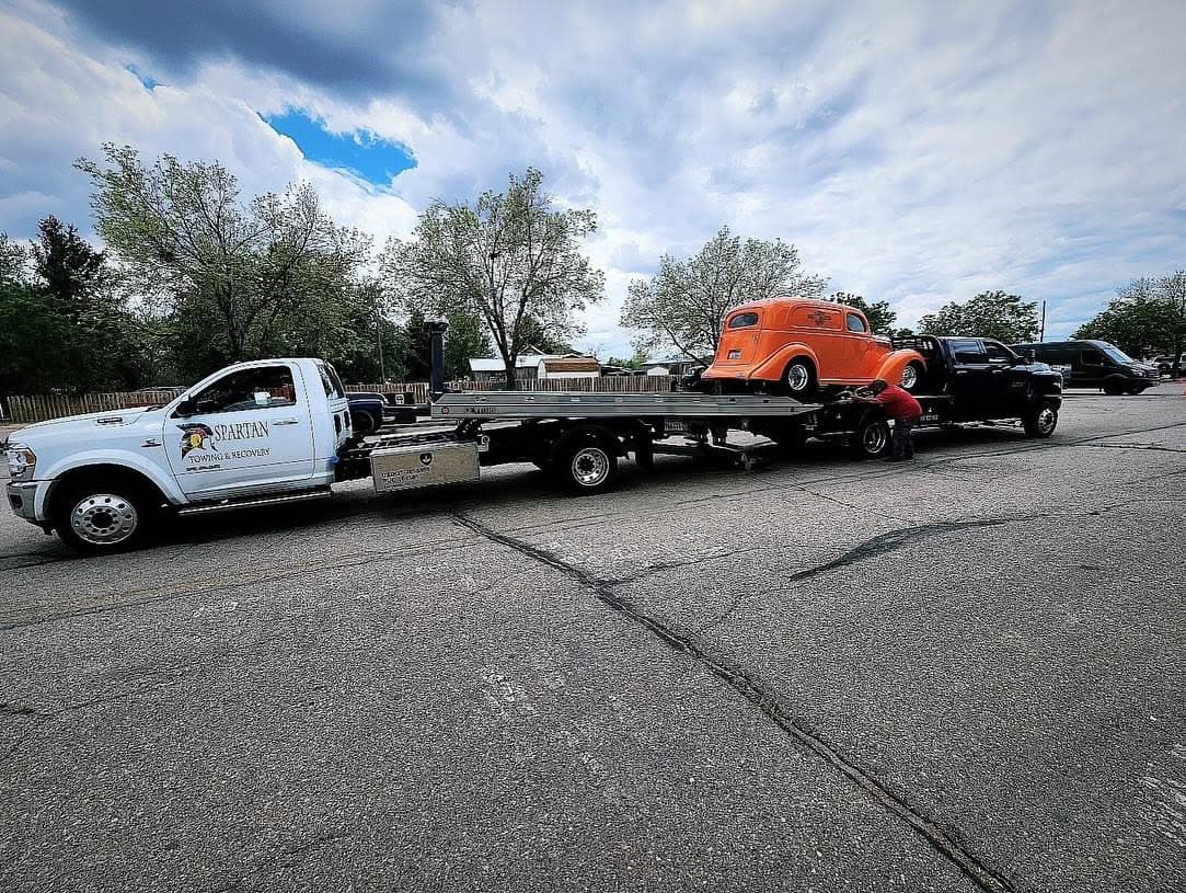 Flatbed carrying an orange vintage truck and a black vehicle